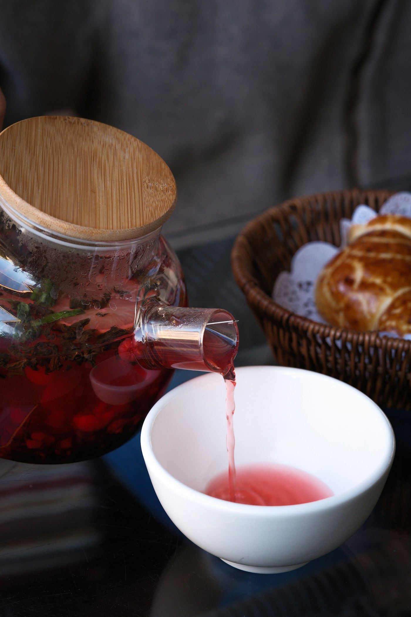 Deep red hibiscus tea being poured from a glass teapot into a small bowl