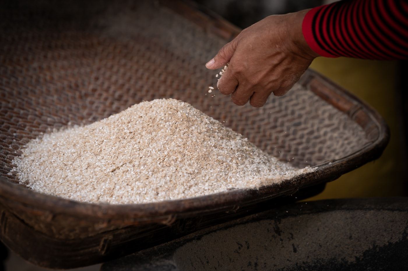 A hand scooping long-grain rice from a woven basket